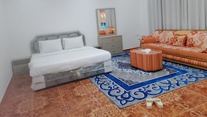 A bedroom with a bed, a sofa, a mirror, and a patterned rug.