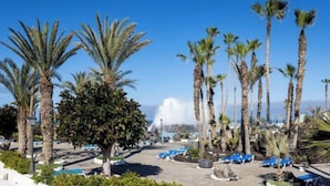 A resort with palm trees, a pool area with lounge chairs, and a clear blue sky. - Vv03. Atardecer Martianez (Puerto de la Cruz)