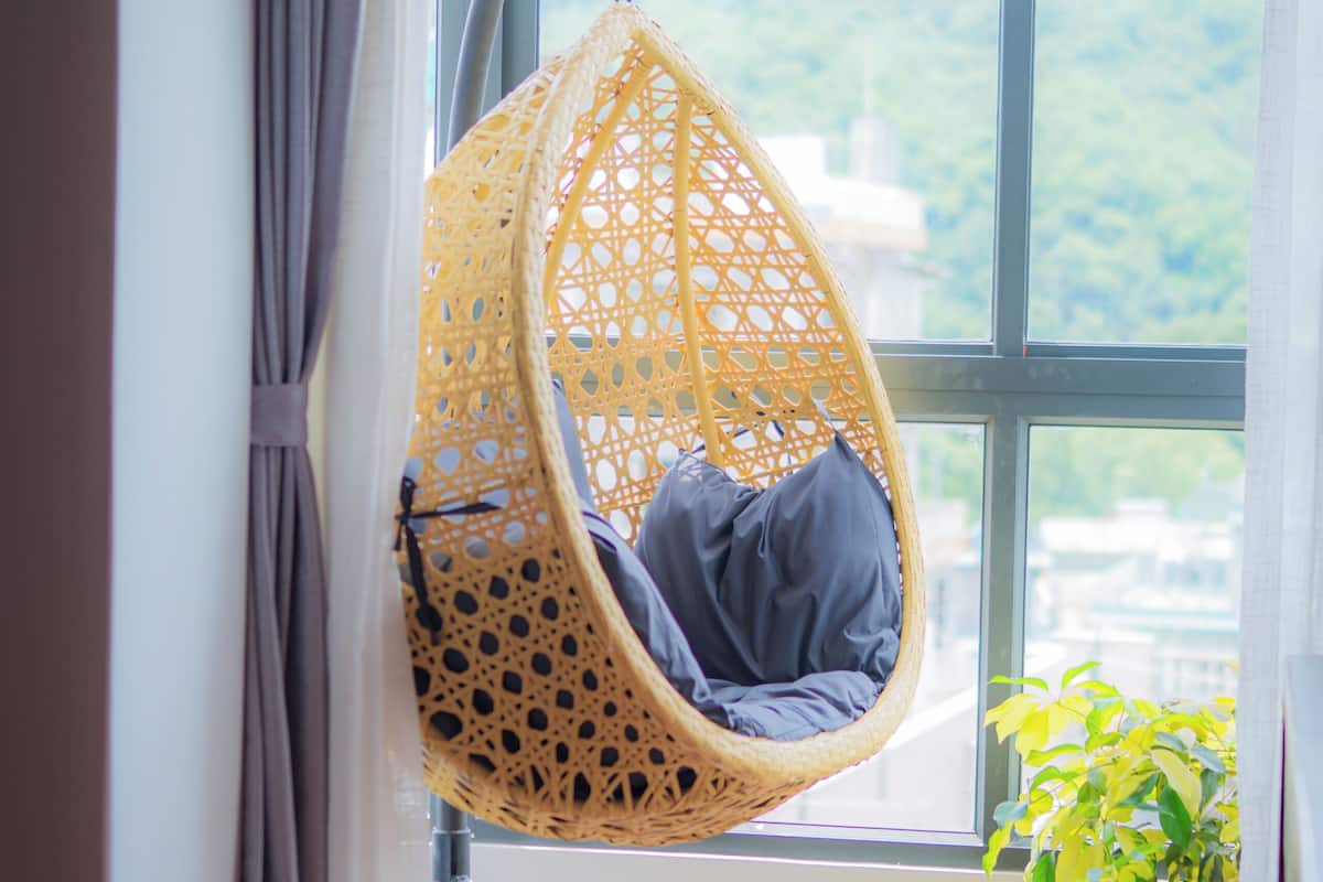 Una habitación con un ventanal grande, una silla colgante y una planta en maceta.