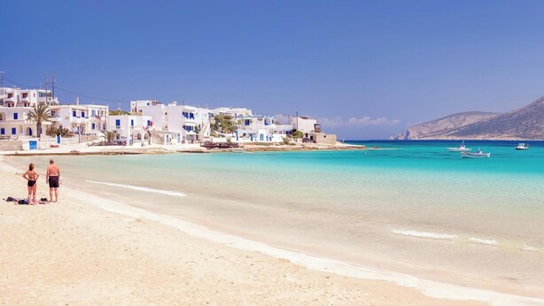 Una playa costera con edificios blancos, agua turquesa cristalina y barcos.
