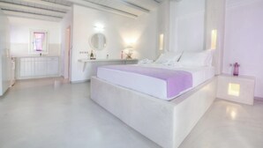 A modern hotel room with a large bed, a vanity with a mirror, and a small seating area.