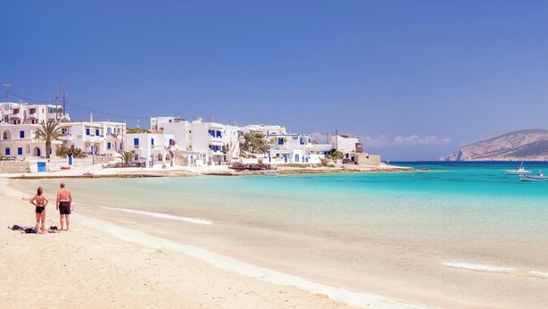 A coastal beach with white buildings, clear turquoise water, and boats.