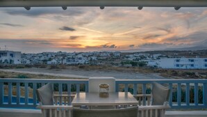 Et bord med stole på en balkon med udsigt over en kystby i solnedgang.