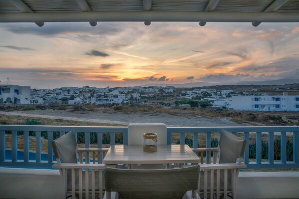 Una mesa con sillas en un balcón con vistas a un pueblo costero al atardecer.