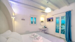 Een slaapkamer met een bed, nachtkastje, spiegel, televisie en een badkamer met douche en raam.