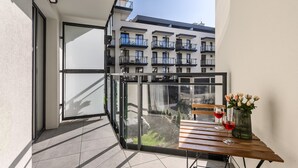 A balcony with a glass door, a wooden table, two wine glasses, and a vase of flowers. - Lumina stylish apart Park Skaryszewski (Warsaw)