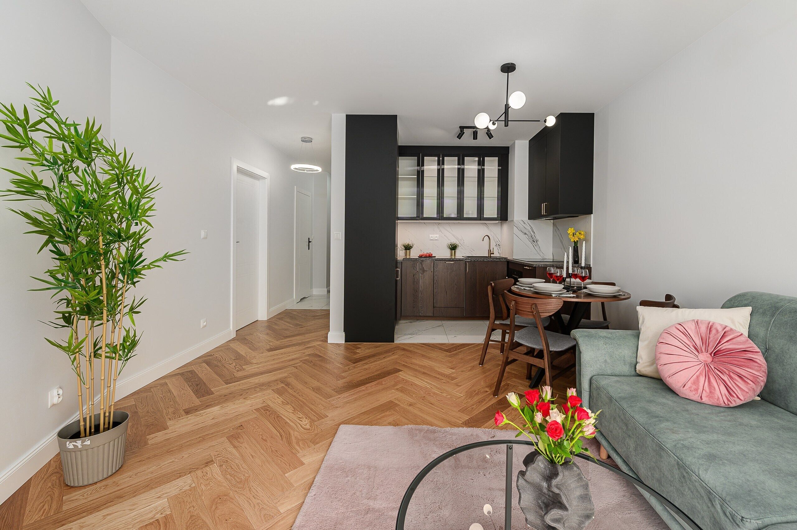 A modern living room with a sofa, a dining table with chairs, a kitchen in the background, and a bamboo plant.