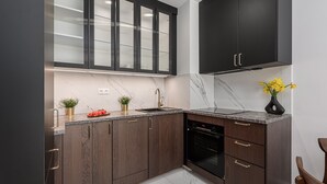 A modern kitchen with dark wood cabinets, a marble countertop, a black oven, and a stainless steel refrigerator. - Lumina stylish apart Park Skaryszewski (Warsaw)