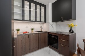Eine moderne Küche mit dunklen Holzschränken, einer Marmorarbeitsplatte, einem schwarzen Backofen und einem Edelstahlkühlschrank.