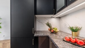 A kitchen with dark cabinets, a marble countertop, a fruit bowl, and a potted plant. - Lumina stylish apart Park Skaryszewski (Warsaw)