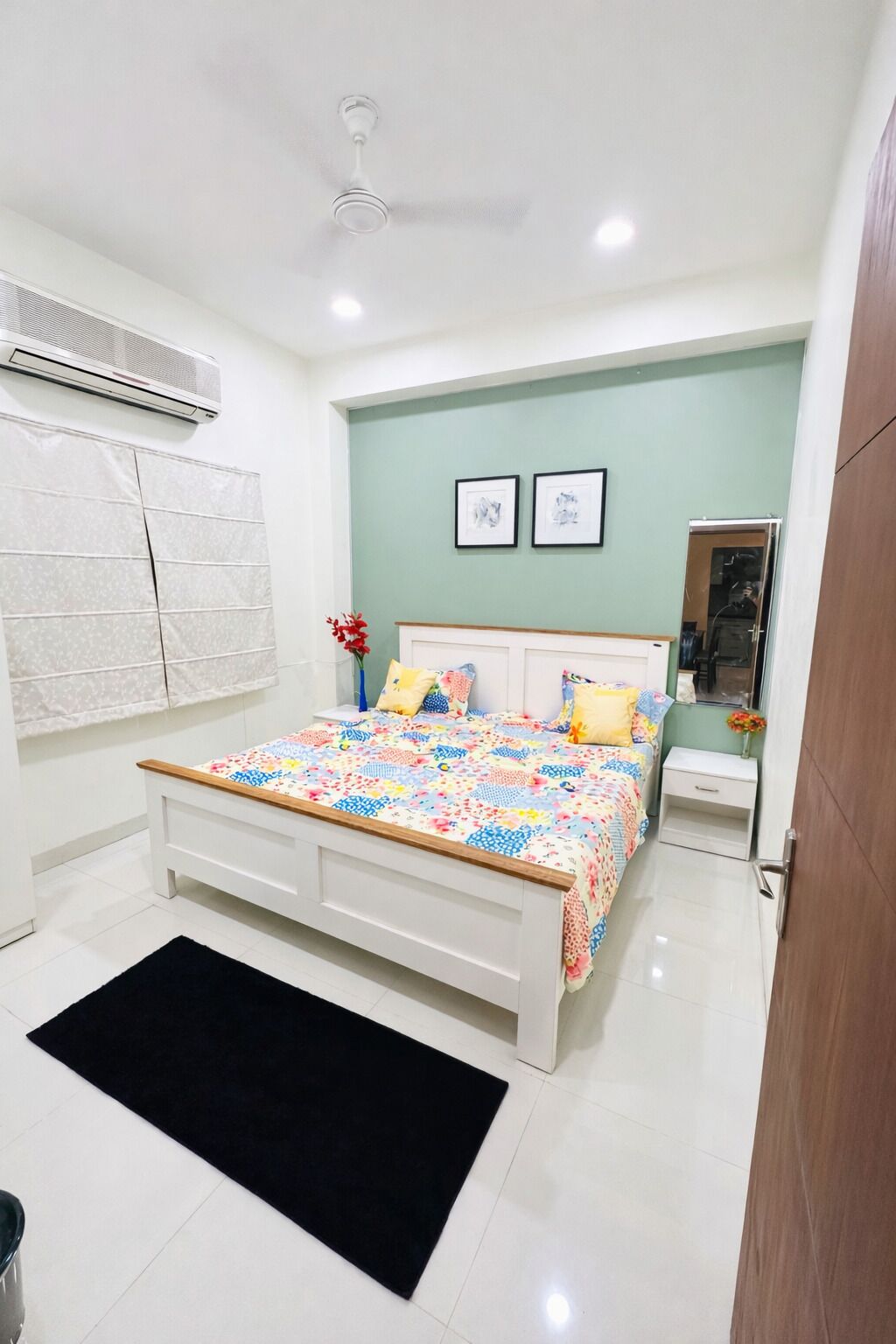 A bedroom with a bed, bedside tables, an air conditioning unit, a black rug, and a wall-mounted air conditioner.