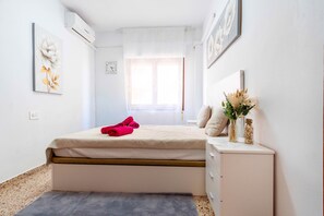 A bedroom with a bed, a bedside table with a vase, a window with curtains, and a wall clock. - BlueCalp: Just 2 minutes from the beach and the boardwalk—Modern living in a prime location in Calp (Calp)