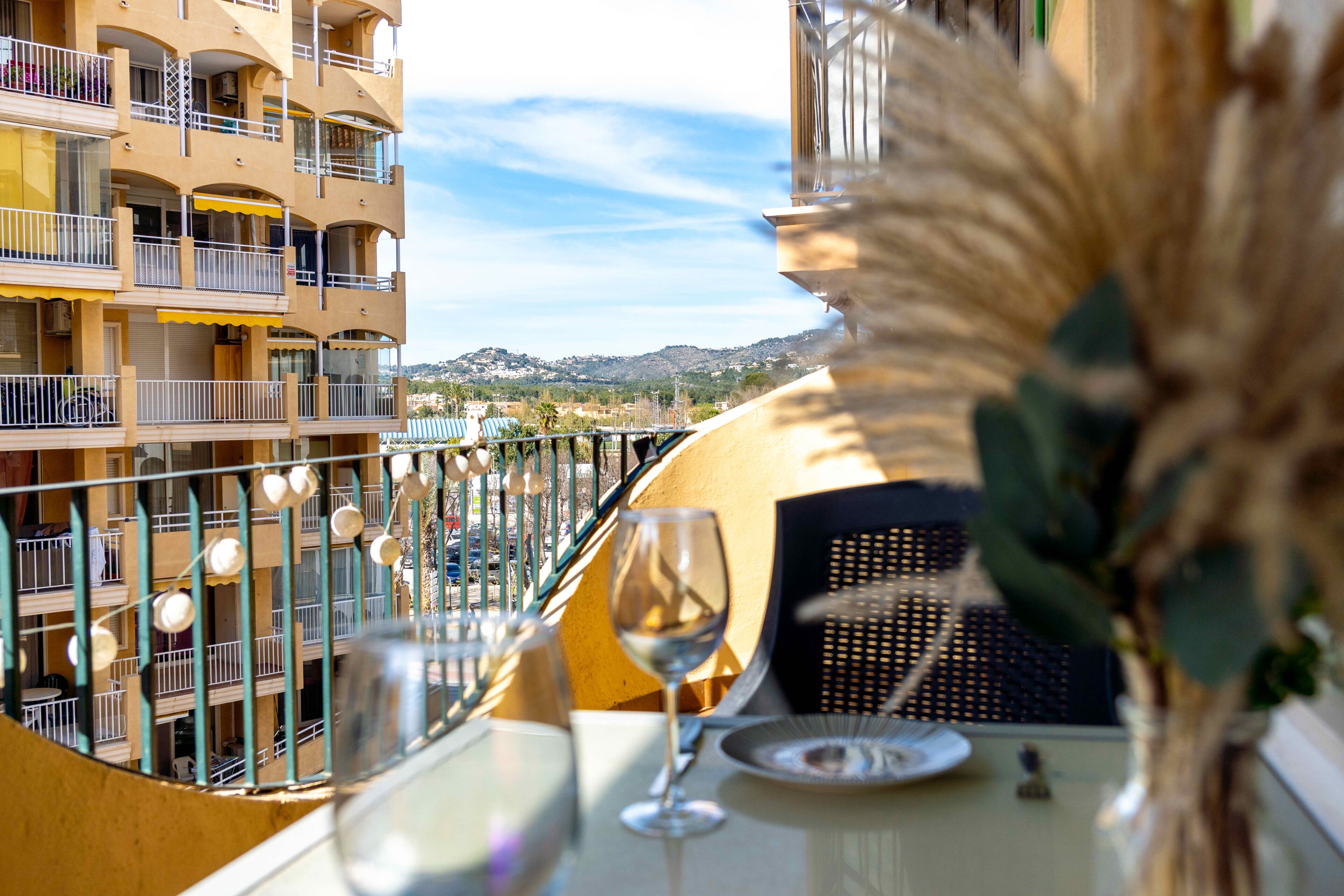 Ein Balkon mit Esstisch, einem Weinglas und Blick auf ein Gebäude mit Balkonen.