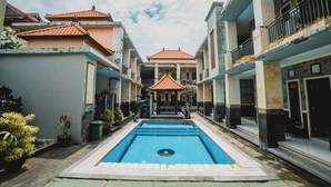 Una piscina con una estructura de techo con azulejos en el centro, rodeada de edificios de varios pisos con balcones.