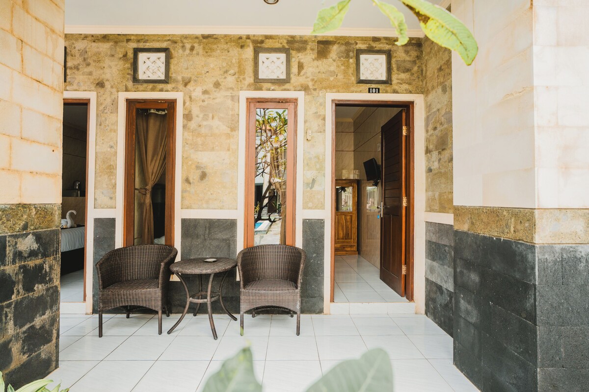 A room with two wicker chairs and a small table, a doorway leading to another room, and a tiled floor.