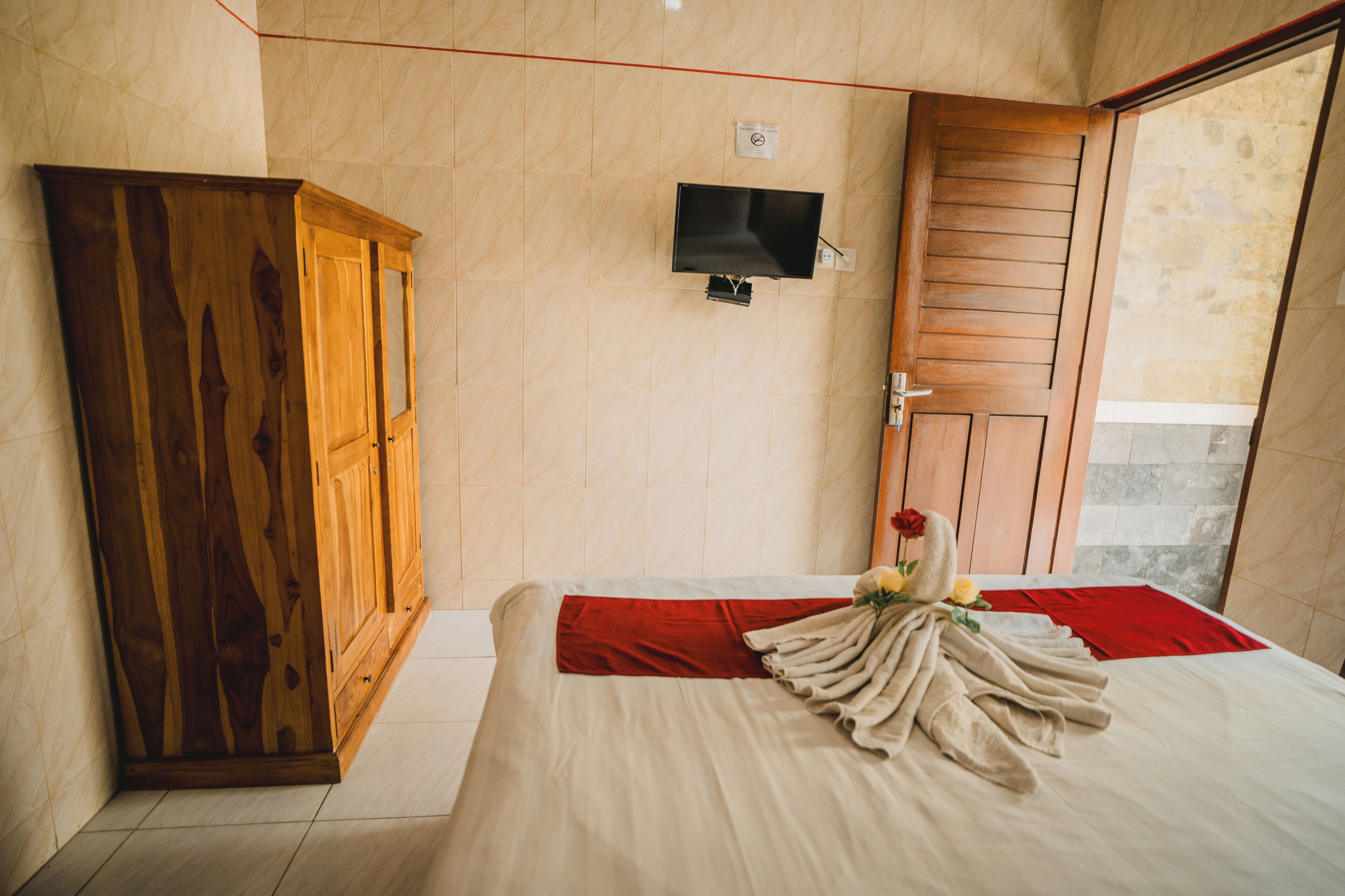 A hotel room with a bed, a wooden wardrobe, a television, and a door.