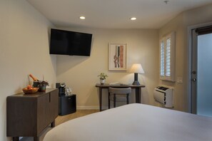 Une chambre d’hôtel comprenant un lit, un bureau avec une chaise, un téléviseur fixé au mur, une fenêtre avec des stores et une porte.