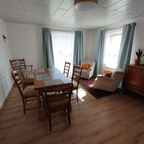 A dining area with a wooden table and chairs, a sofa, and a cabinet with a plant. - Cozy vacation home in the village with its own garden (Gottesgabe)