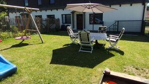 Un patio trasero con un columpio, una mesa con sillas y una zona de juegos con arena y juguetes.