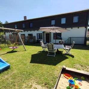 Ein Garten mit Schaukel, Tisch mit Stühlen und einem Spielbereich mit Sand und Spielzeug.
