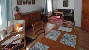 Una sala de estar con sofá, una mesa de comedor con individuales, un aparador de madera y un lámpara en el techo.