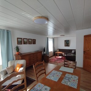 Ein Wohnzimmer mit einer Couch, einem Esstisch mit Platzsets, einem Holzschrank und einer Deckenleuchte.