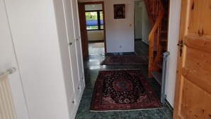 Un pasillo con una escalera de madera, un armario blanco y una alfombra estampada.