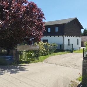 Ein zweistöckiges Gebäude mit dunklem Dach und weißen Wänden, einer gepflasterten Auffahrt und einem Metallzaun.
