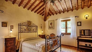 Un dormitorio con techo de madera, una cama con estructura metálica, una mesita de noche, un aparador y una ventana con cortinas.