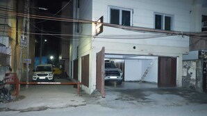 Un área de estacionamiento cerrada con un coche blanco dentro, una motocicleta fuera y un edificio con un letrero que dice 'XI-XII Knowledge Institute'.