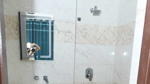 Un baño con lavamanos, espejo, ducha, inodoro y un cubo rojo.