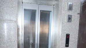 Un ascensor con acabado metálico, una pantalla digital y un panel de control con un botón rojo.