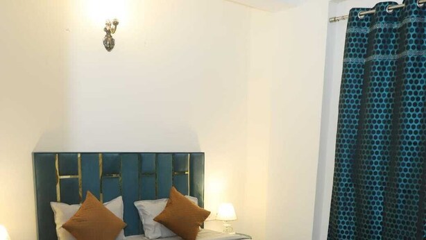 Un dormitorio con cama, mesitas de noche, lámpara y cortina.