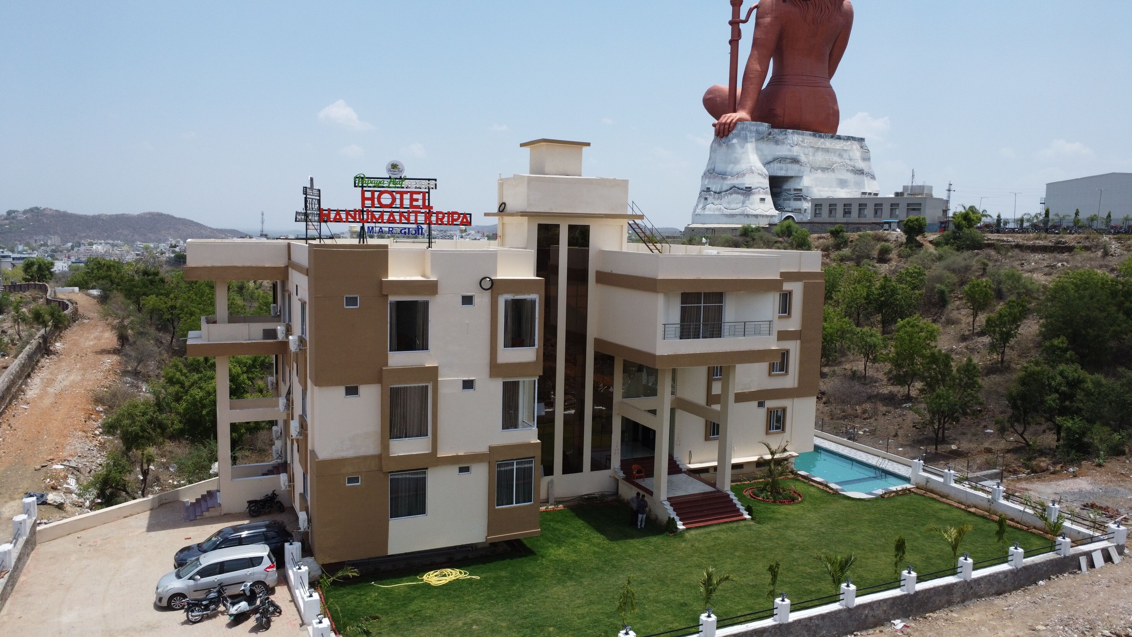 A modern hotel with a swimming pool, a large statue, and a sign indicating it is a hotel.