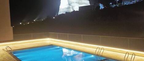 Vista nocturna de una piscina con una estatua al fondo.