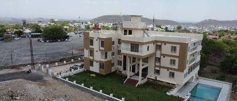 A multi-story building with a flat roof, a swimming pool, and a parking lot.
