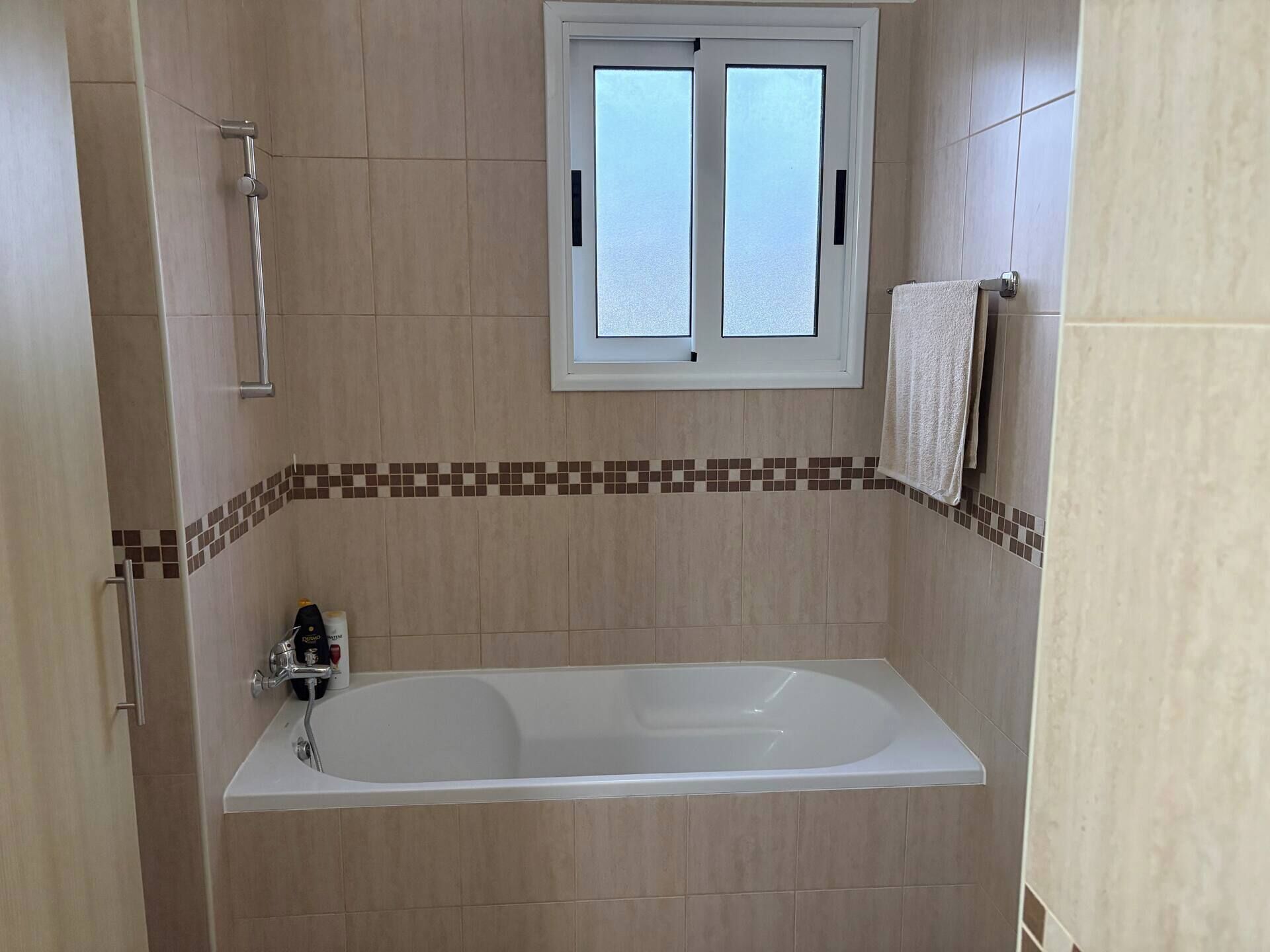 A bathroom with a bathtub, a window, and a towel rack.