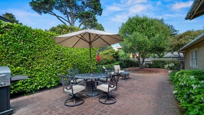 Eine Terrasse mit Tisch, Stühlen, einem Grill und einer Hecke.