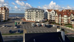 A coastal residential area with multi-story buildings, a parking lot, and a view of the sea. - Soley with parking by Interhome (De Haan)