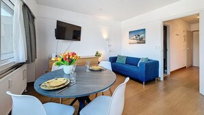 A modern living room with a round table, blue sofa, and a flat-screen TV mounted on the wall. - Soley with parking by Interhome (De Haan)