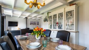 A dining room with a wooden table set for four, a chandelier, and a cabinet with glass doors. - Alice Blue with airco & shared pool by Interhome (De Haan)