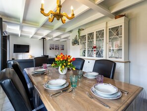 A dining room with a wooden table set for four, a chandelier, and a cabinet with glass doors. - Alice Blue with airco & shared pool by Interhome (De Haan)