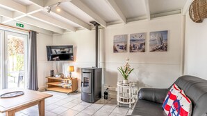A living room with a sofa, a TV, a fireplace, a small table, and artwork on the wall. - Alice Blue with airco & shared pool by Interhome (De Haan)