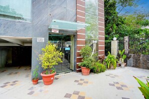 Entrada de hotel con puerta de vidrio, plantas en macetas y piso de baldosas.