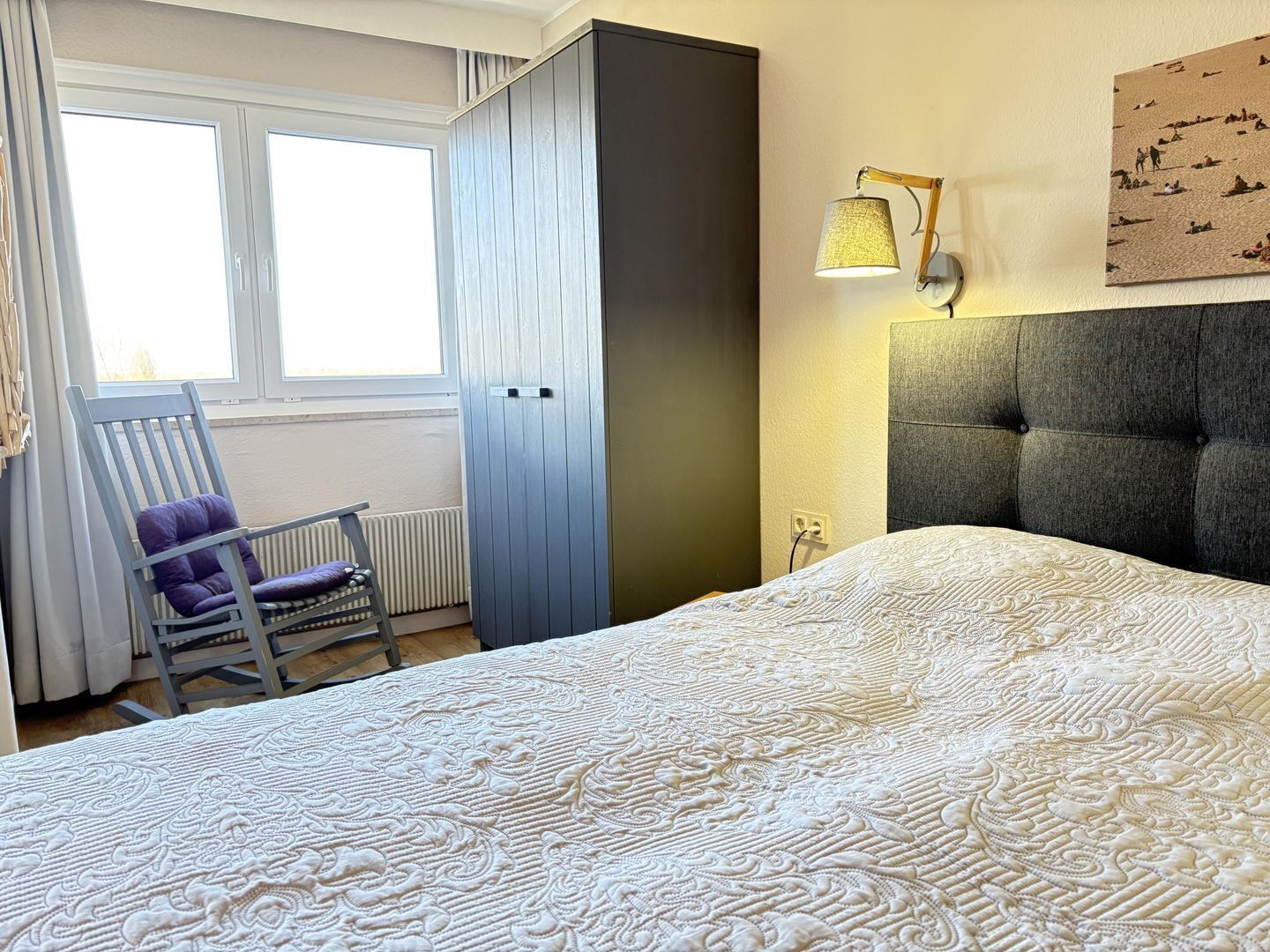 Une chambre à coucher comprenant un lit, une chaise, une armoire, une lampe fixée au mur et une fenêtre.