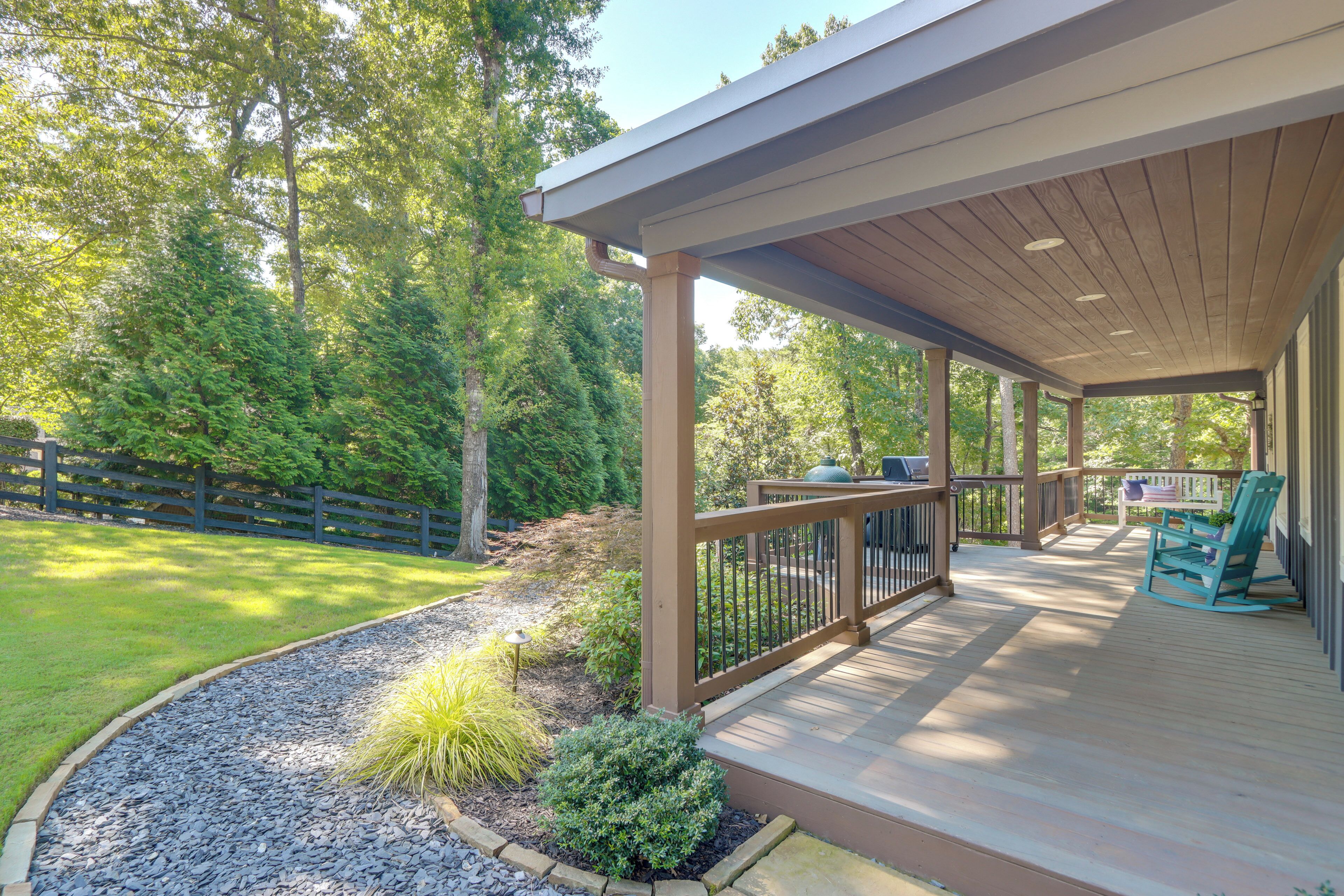 A covered deck with a railing, a small table with chairs, and a view of a wooded area.