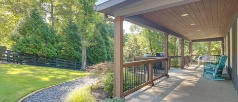 A covered deck with a railing, a small table with chairs, and a view of a wooded area.