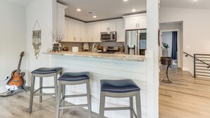 A modern kitchen with white cabinets, a stainless steel refrigerator, and a bar area with stools. - Boat Dock + Yard: Lake Lanier Gem in Gainesville (Gainesville)