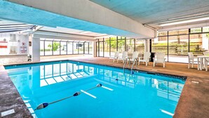 En inomhuspool med klart vatten, vita stolar och bord runt poolområdet.