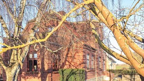 A brick building with a stone foundation, surrounded by trees and a well-maintained garden.